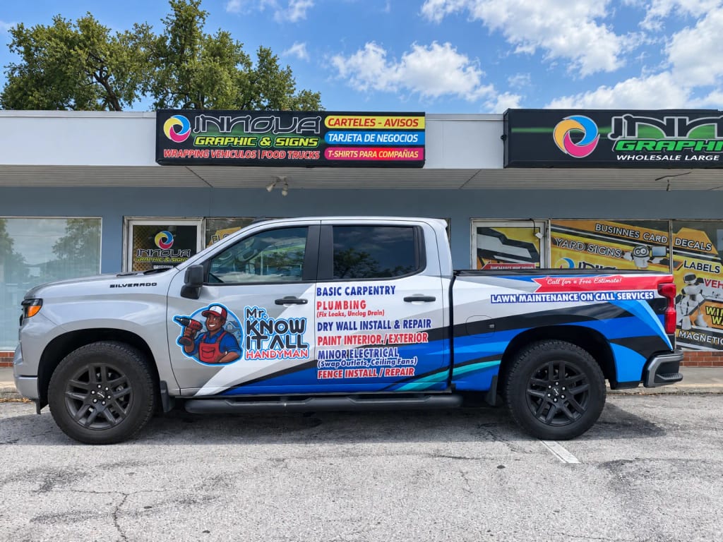 Pickup plateada con wrap parcial azul y rojo de un servicio de handyman frente al taller de Innova