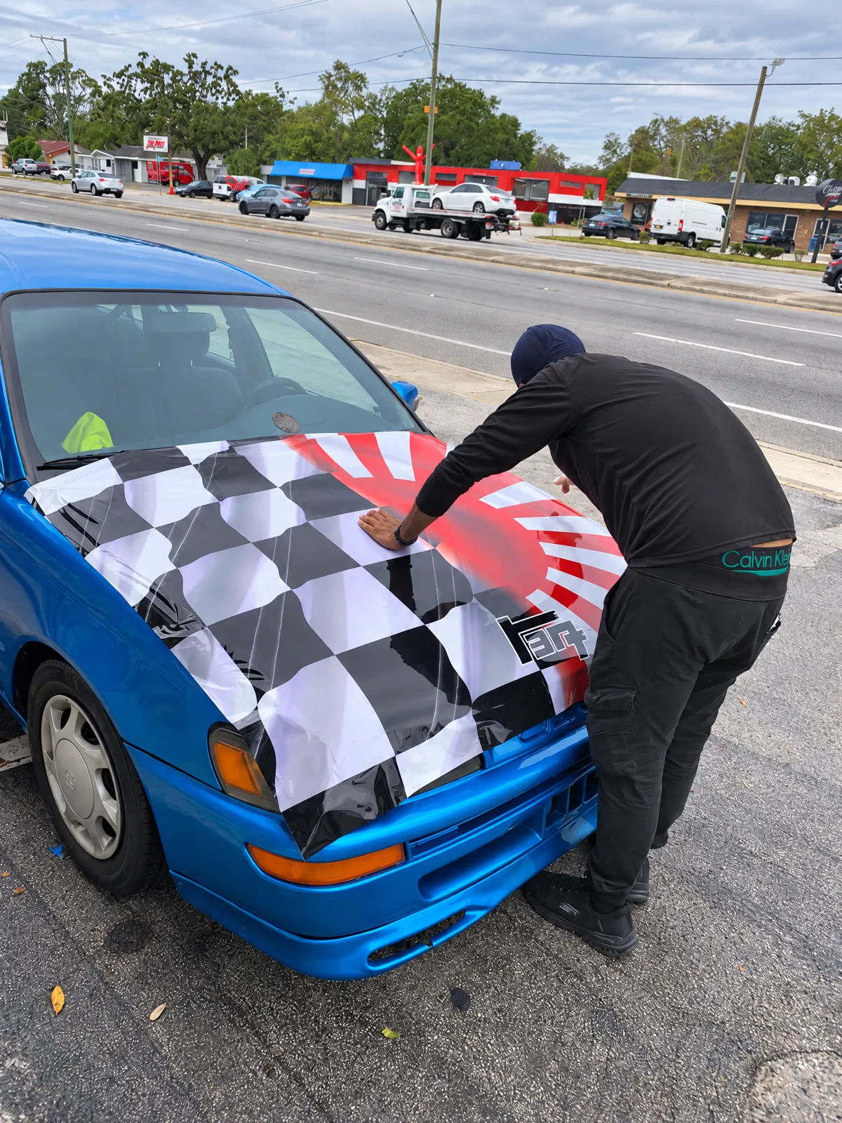 Instalador de Innova poniendo un wrap de cuadros y sol naciente en el cofre de un carro azul